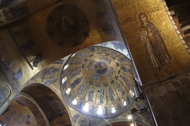 Two mosaic domes and a standing saint on a gold ground, seen from the floor of the church