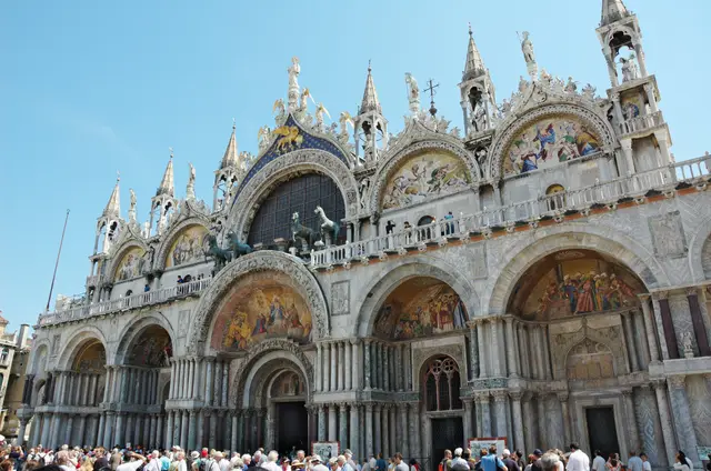 The west front of St Mark’s Basilica, Venice: gold mosaics in the arches, the bronze horses on the loggia and visitors in the square below