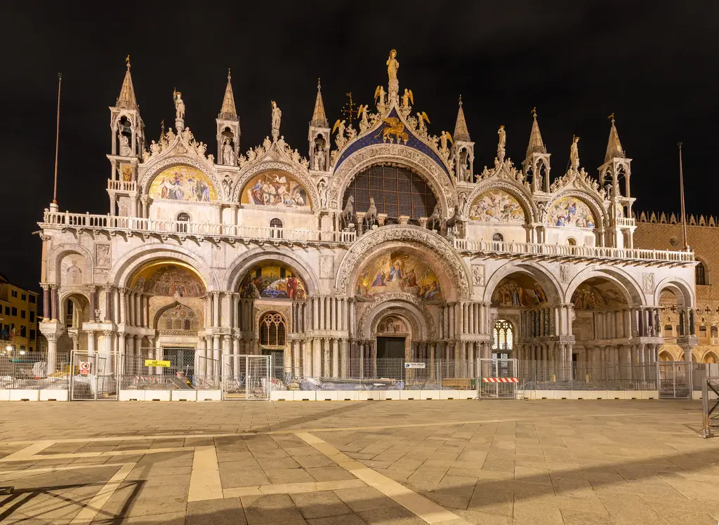 The west front of St Mark’s lit at night, its gold mosaics glowing in the arches