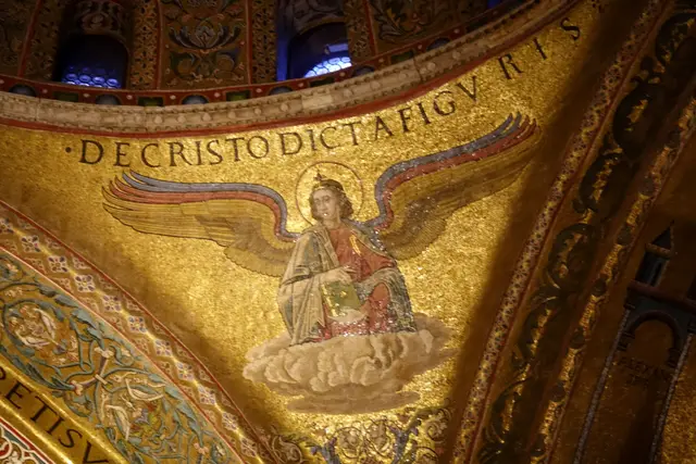 A winged figure holding a book, in a gold mosaic under a Latin inscription